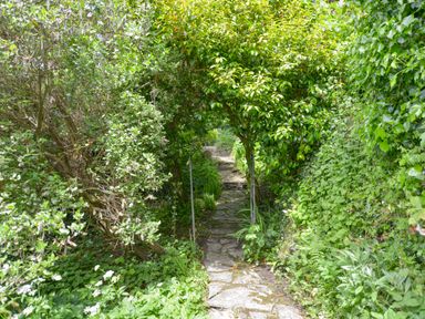 A stone pathway with an arch covered in greenery in a garden at Little Gate Cottage in North Bovey