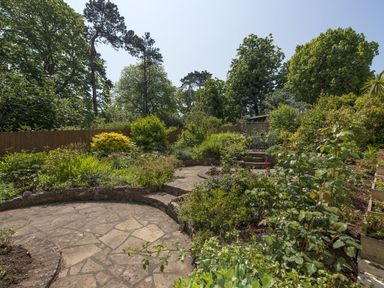 A garden with a stone patio surrounded by plants and trees at Exe View in Dawlish