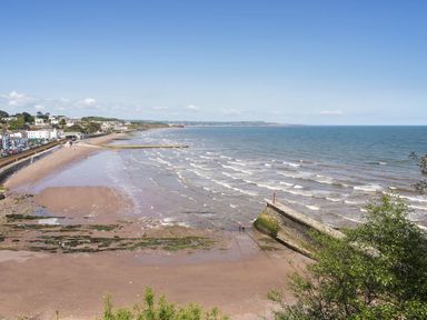 A beach with waves and a stone pier with houses and a road along the shore at Exe View in Dawlish