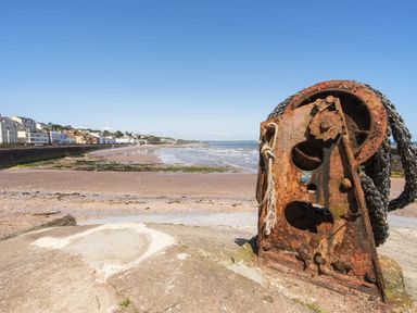 A rusted metal winch with rope on a concrete surface near a beach with a row of houses in the background at Exe View in Dawlish