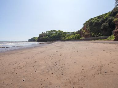A sandy beach with scattered stones and a rocky cliff with greenery at Exe View in Dawlish
