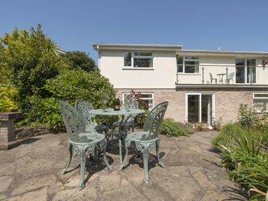 A patio with a metal table and four chairs with a bottle and glasses in a garden at Exe View in Dawlish