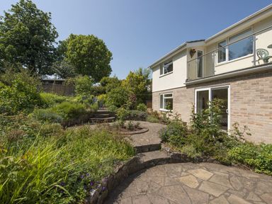A garden with stone steps and patio next to a two story house with balcony at Exe View in Dawlish