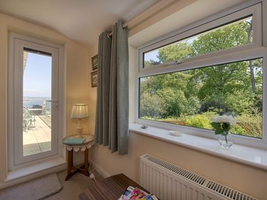 A corner of a room with a window showing trees and a door leading to a patio at Exe View in Dawlish