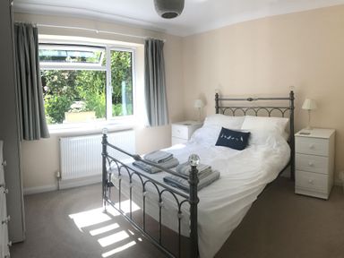 A bedroom with a metal bed frame white bedding two white bedside tables with lamps and a window with curtains at Exe View in Dawlish