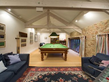 A game room with a pool table two sofas a foosball table and framed pictures on the wall at Sandridge Barton in Stoke Gabriel