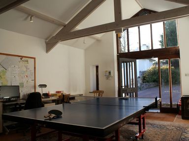 A room with a ping pong table in the center and desks with chairs and a computer along the wall at Sandridge Barton in Stoke Gabriel