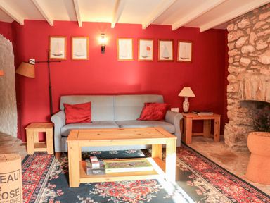 A living room with a blue sofa and red cushions wooden tables a stone fireplace and framed pictures on a red wall at Sandridge Barton in Stoke Gabriel