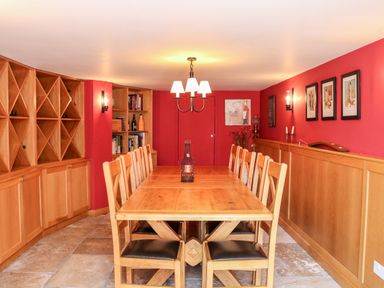 A dining room with a wooden table and chairs with red walls and built in wooden shelves at Sandridge Barton in Stoke Gabriel
