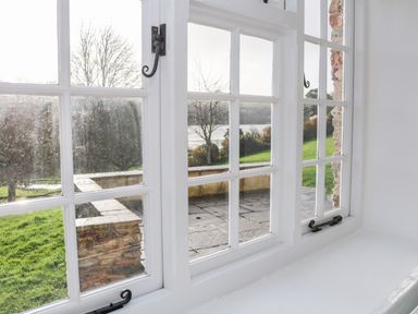 A view through white framed windows showing a stone patio and green lawn with trees at Sandridge Barton in Stoke Gabriel