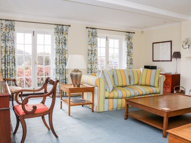 A living room with striped sofa wooden chairs coffee table and side table with lamp at Sandridge Barton in Stoke Gabriel