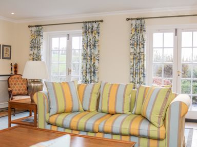 A living room with a striped sofa and patterned curtains at Sandridge Barton in Stoke Gabriel
