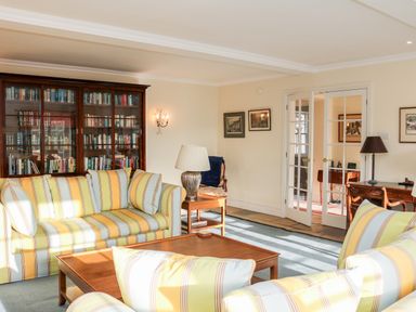 A living room with striped sofas a wooden coffee table a glass door bookcase and framed pictures on the walls at Sandridge Barton in Stoke Gabriel