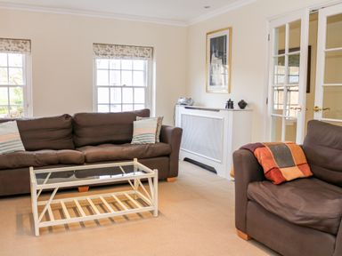 A sitting room with two brown sofas a glass coffee table and a white radiator cover at Sandridge Barton in Stoke Gabriel