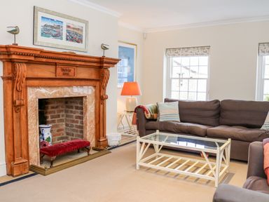 A living room with a wooden fireplace brown sofas glass coffee table and windows at Sandridge Barton in Stoke Gabriel