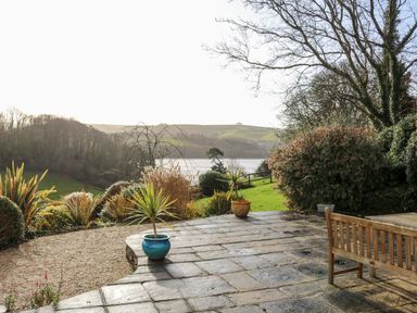 An outdoor patio with potted plants a wooden table and bench overlooking a lake and hills at Sandridge Barton in Stoke Gabriel