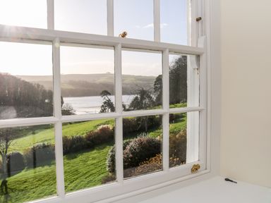 A window with white frame looking out to a grassy garden and river beyond at Sandridge Barton in Stoke Gabriel