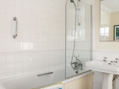 A bathroom with a bathtub shower combination a white pedestal sink and a mirror at Sandridge Barton in Stoke Gabriel