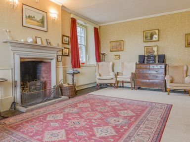 A sitting room with a fireplace three armchairs a wooden chest of drawers and a patterned rug at Wootton House in Butleigh Wootton near Compton Dundon