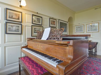 A piano with sheet music on a stand in a room with framed pictures on the walls at Wootton House in Butleigh Wootton near Compton Dundon
