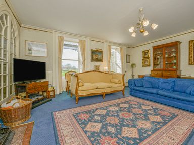 A living room with blue and yellow sofas a patterned rug a wooden cabinet and a TV at Wootton House in Butleigh Wootton near Compton Dundon