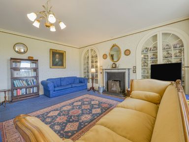 A living room with a blue sofa a yellow sofa a bookshelf a fireplace and built in cabinets with plates at Wootton House Butleigh Wootton near Compton Dundon