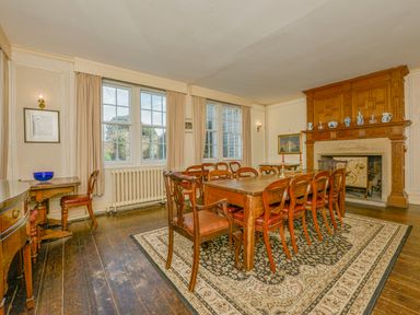 A dining room with a wooden table and chairs on a patterned rug near a fireplace at Wootton House in Butleigh Wootton near Compton Dundon