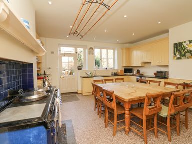 A kitchen with wooden table and chairs blue stove cream cabinetry and windows at Wootton House in Butleigh Wootton near Compton Dundon