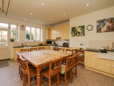 A kitchen with wooden table and chairs and yellow cabinets at Wootton House in Butleigh Wootton near Compton Dundon