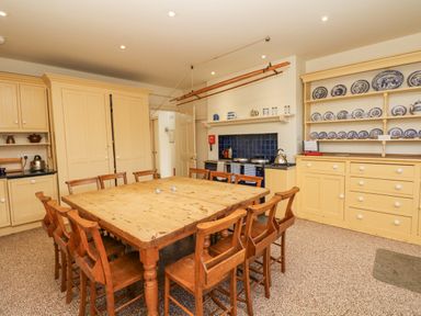 A kitchen with a wooden dining table and chairs yellow cabinets blue tiled stove and a cabinet with blue and white plates at Wootton House in Butleigh Wootton near Compton Dundon