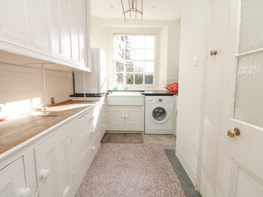 A narrow kitchen with white cabinets a wooden countertop a washing machine and a window at Wootton House in Butleigh Wootton near Compton Dundon
