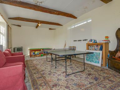 A game room with a ping pong table, red sofas, a pool table, bookshelf, and wooden ceiling beams at Wootton House in Butleigh Wootton near Compton Dundon