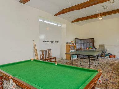A game room with a pool table, a ping pong table, two wooden chairs, a bookshelf, and wooden ceiling beams at Wootton House in Butleigh Wootton near Compton Dundon