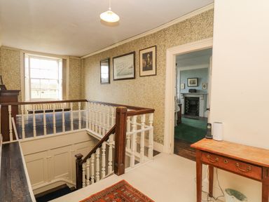 A hallway with a carpeted floor a wooden table and framed pictures on the wall at Wootton House Butleigh Wootton near Compton Dundon
