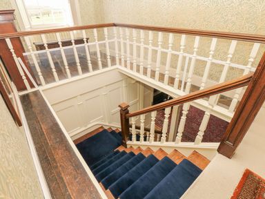 A staircase with blue carpet and white wooden railings in a house with patterned wallpaper at Wootton House in Butleigh Wootton near Compton Dundon