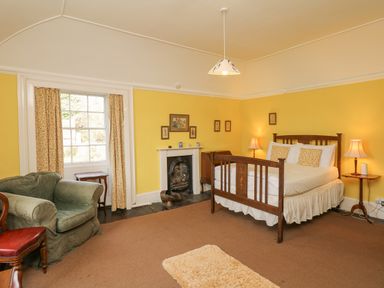 A bedroom with yellow walls a wooden bed green armchair and a fireplace at Wootton House in Butleigh Wootton near Compton Dundon