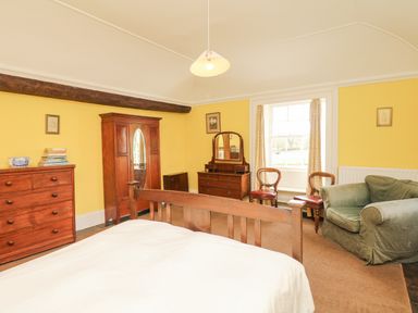 A bedroom with wooden furniture including a bed, dresser, wardrobe, chairs, and a green armchair at Wootton House in Butleigh Wootton near Compton Dundon