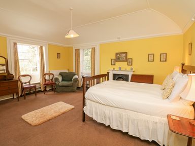 A bedroom with a wooden bed and white bedding yellow walls a fireplace two chairs and an armchair at Wootton House in Butleigh Wootton near Compton Dundon
