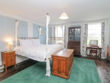 A bedroom with a four poster bed wooden furniture green carpet and two windows with floral curtains at Wootton House in Butleigh Wootton near Compton Dundon