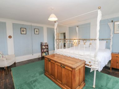 A bedroom with a four-poster bed wooden chest green carpet bookshelf and armchair at Wootton House in Butleigh Wootton near Compton Dundon