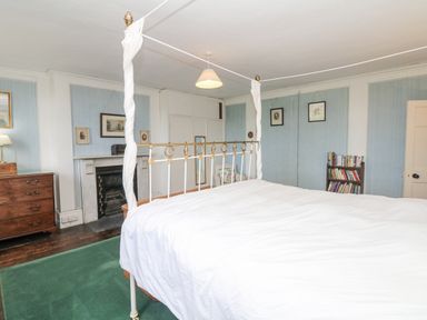 A bedroom with a four-poster bed a chest of drawers a fireplace a bookshelf and framed pictures on the walls at Wootton House in Butleigh Wootton near Compton Dundon