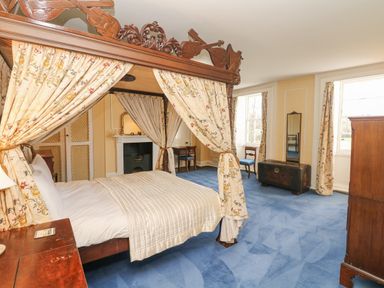 A bedroom with a four poster bed with floral curtains a fireplace two windows a mirror and wooden furniture at Wootton House in Butleigh Wootton near Compton Dundon