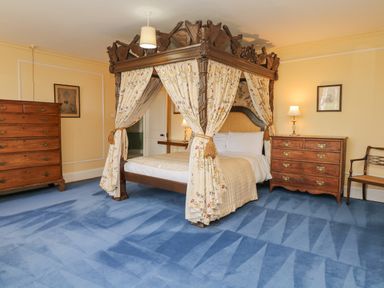 A bedroom with a four poster bed and wooden dressers on a blue carpet at Wootton House in Butleigh Wootton near Compton Dundon