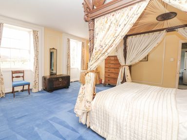 A bedroom with a four-poster bed, blue carpet, wooden chest and chair at Wootton House in Butleigh Wootton near Compton Dundon