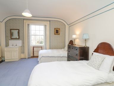 A bedroom with two single beds a chest of drawers a window with curtains and a sink at Wootton House in Butleigh Wootton near Compton Dundon