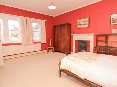 A bedroom with red wallpaper a wooden wardrobe a chair a fireplace a wooden desk and a bed at Wootton House in Butleigh Wootton near Compton Dundon