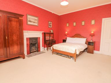 A bedroom with a wooden bed a wooden wardrobe a fireplace and a desk with a chair at Wootton House in Butleigh Wootton near Compton Dundon