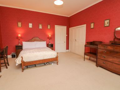 A bedroom with a wooden bed, bedside tables with lamps, a wooden dresser, and red patterned wallpaper at Wootton House in Butleigh Wootton near Compton Dundon