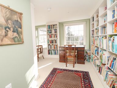 A room with bookshelves along two walls a wooden desk and chair below a window and a framed painting on the wall at Wootton House in Butleigh Wootton near Compton Dundon