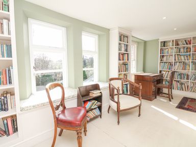 A study room with wooden chairs a wooden desk and bookshelves filled with books at Wootton House in Butleigh Wootton near Compton Dundon